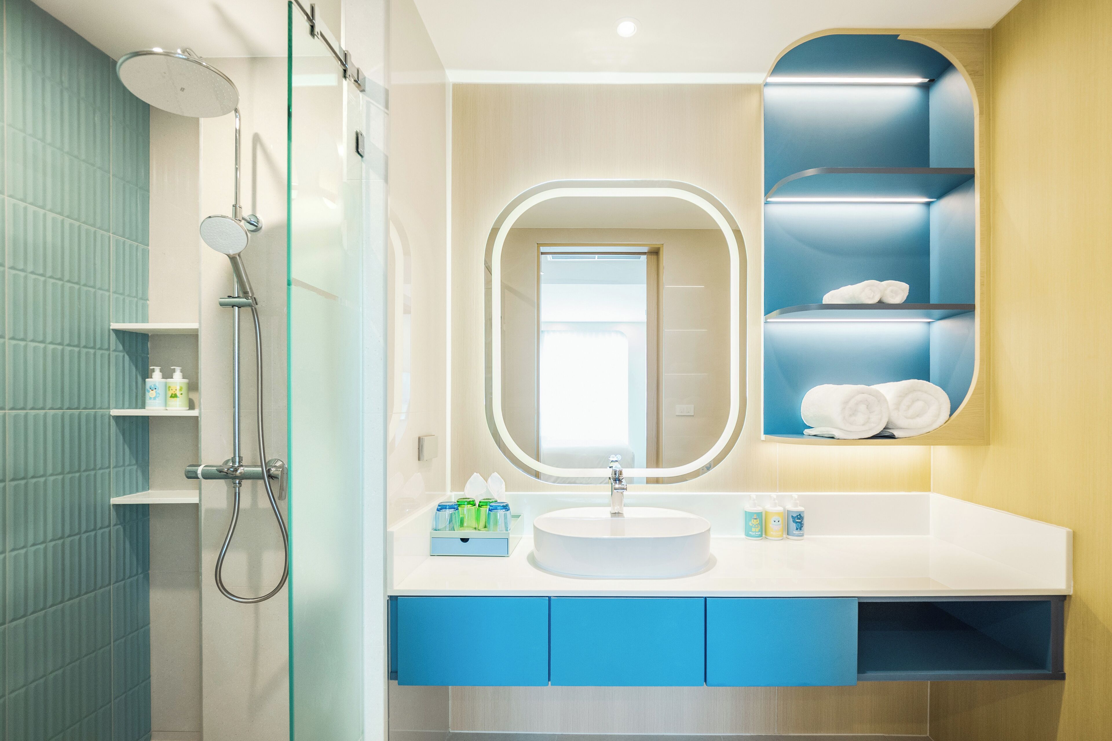 Ein modernes Badezimmer mit einer Duschkabine aus Glas, einem weißen Waschbecken, blauen Schränken und einem Spiegel mit blauem Rahmen.