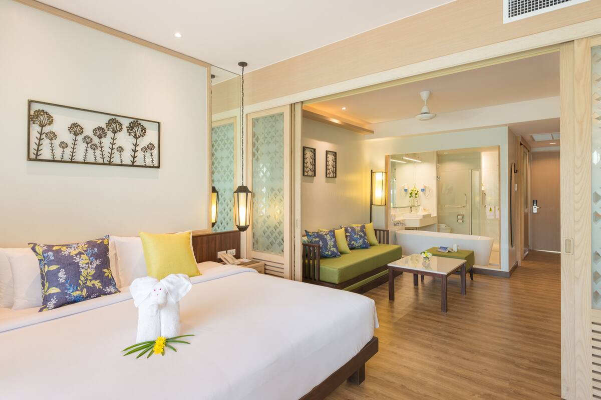 Ein Hotelzimmer mit einem großen Bett, einer Couch, einem kleinen Tisch und einem durch eine offene Tür einsehbaren Badezimmer.