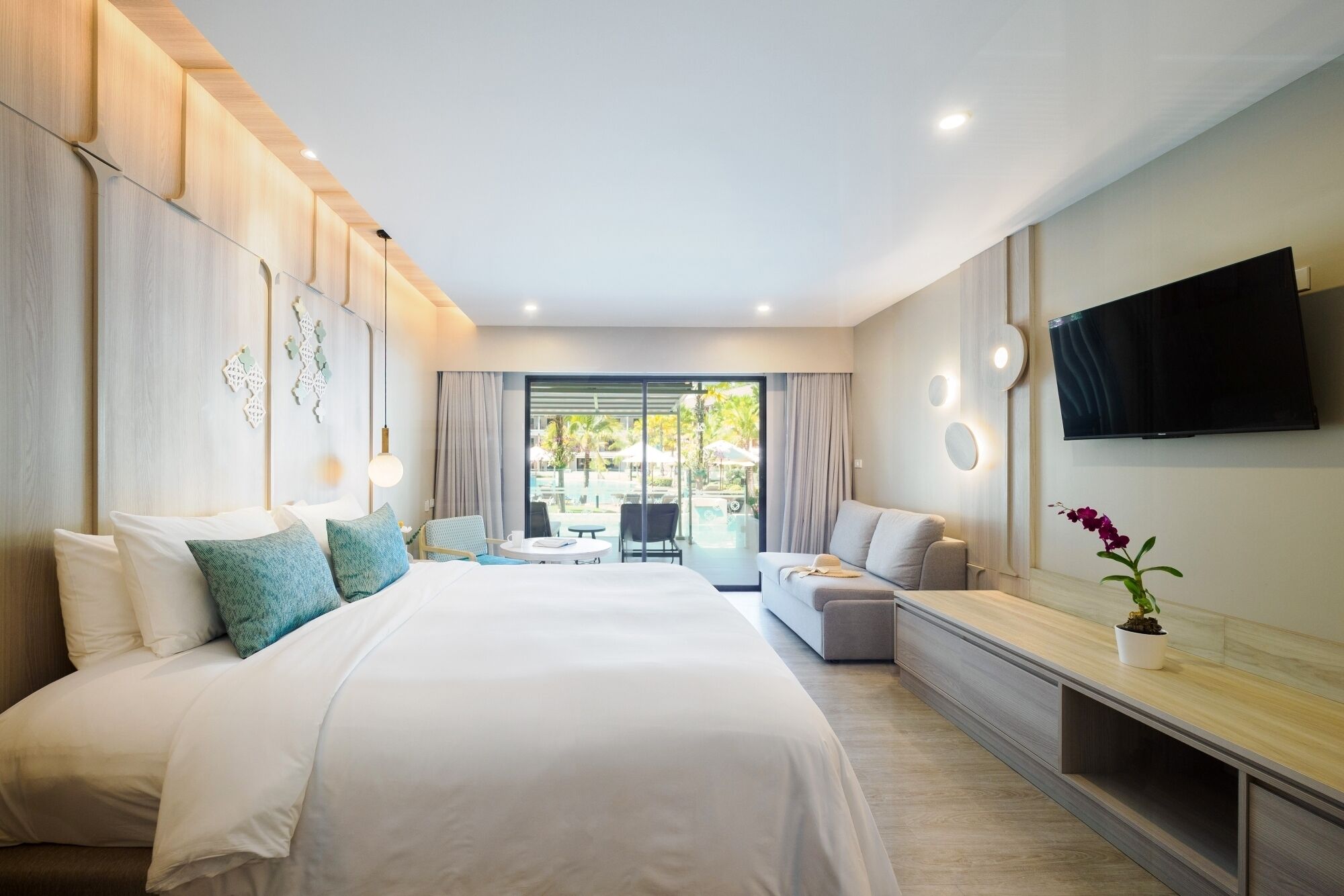 Habitación de hotel moderna con una cama grande, un sofá, un televisor y un balcón con mobiliario exterior.