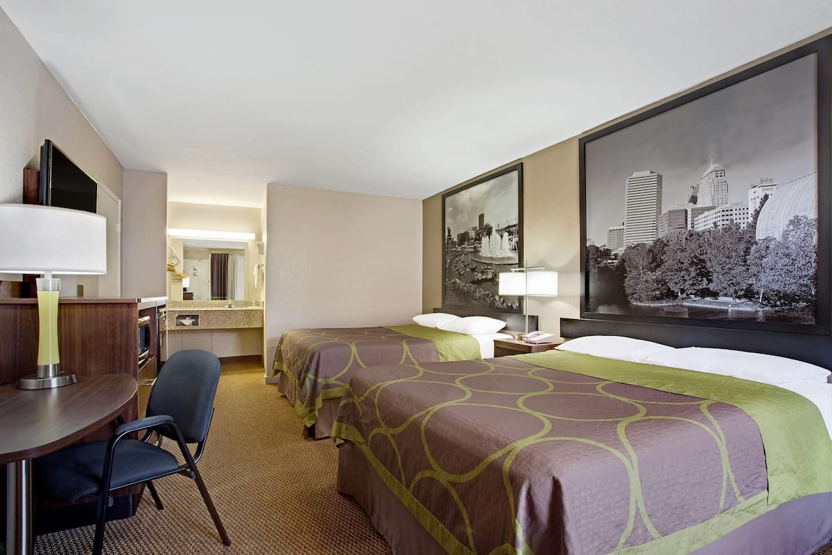 A hotel room with two beds, a desk, a chair, a large window, and a cityscape view.