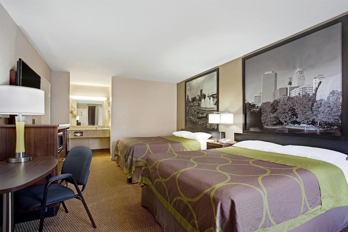 Habitación de hotel con dos camas, un escritorio, una silla, un espejo y dos grandes cuadros con vistas a la ciudad.