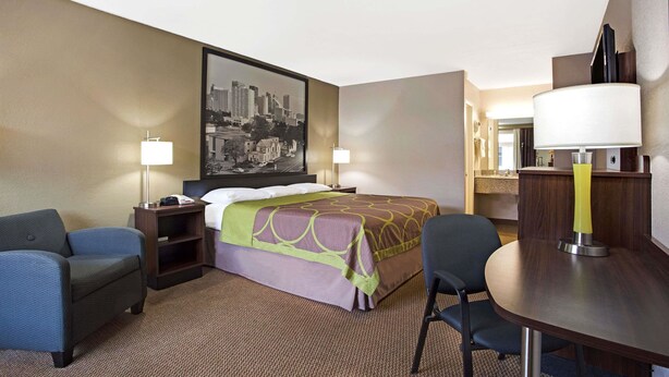 A hotel room with a bed, two chairs, a desk, and a large cityscape painting on the wall. - Super 8 by Wyndham Oklahoma/Frontier City (Oklahoma City)