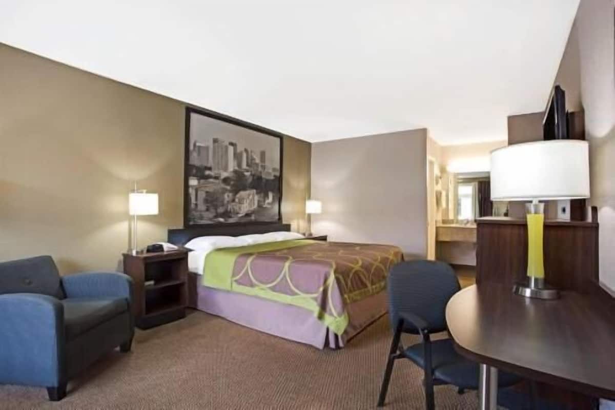 A hotel room with a bed, two bedside tables, a desk with a chair, a lamp, and a large framed picture on the wall.