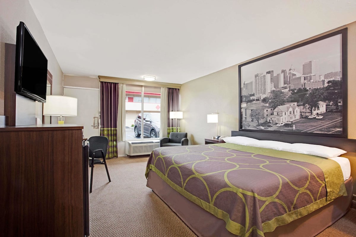 A hotel room with a bed, a desk, a chair, a television, and a large window with curtains.