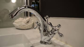 Un baño con grifo de cromo, dispensador de jabón y una cesta de artículos de aseo.