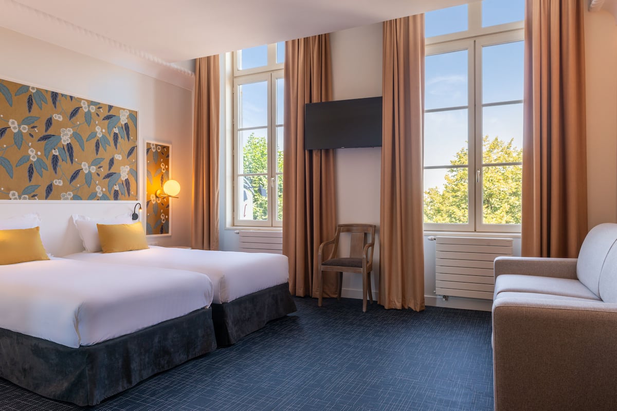A hotel room with two beds, a TV, a chair, and a couch.