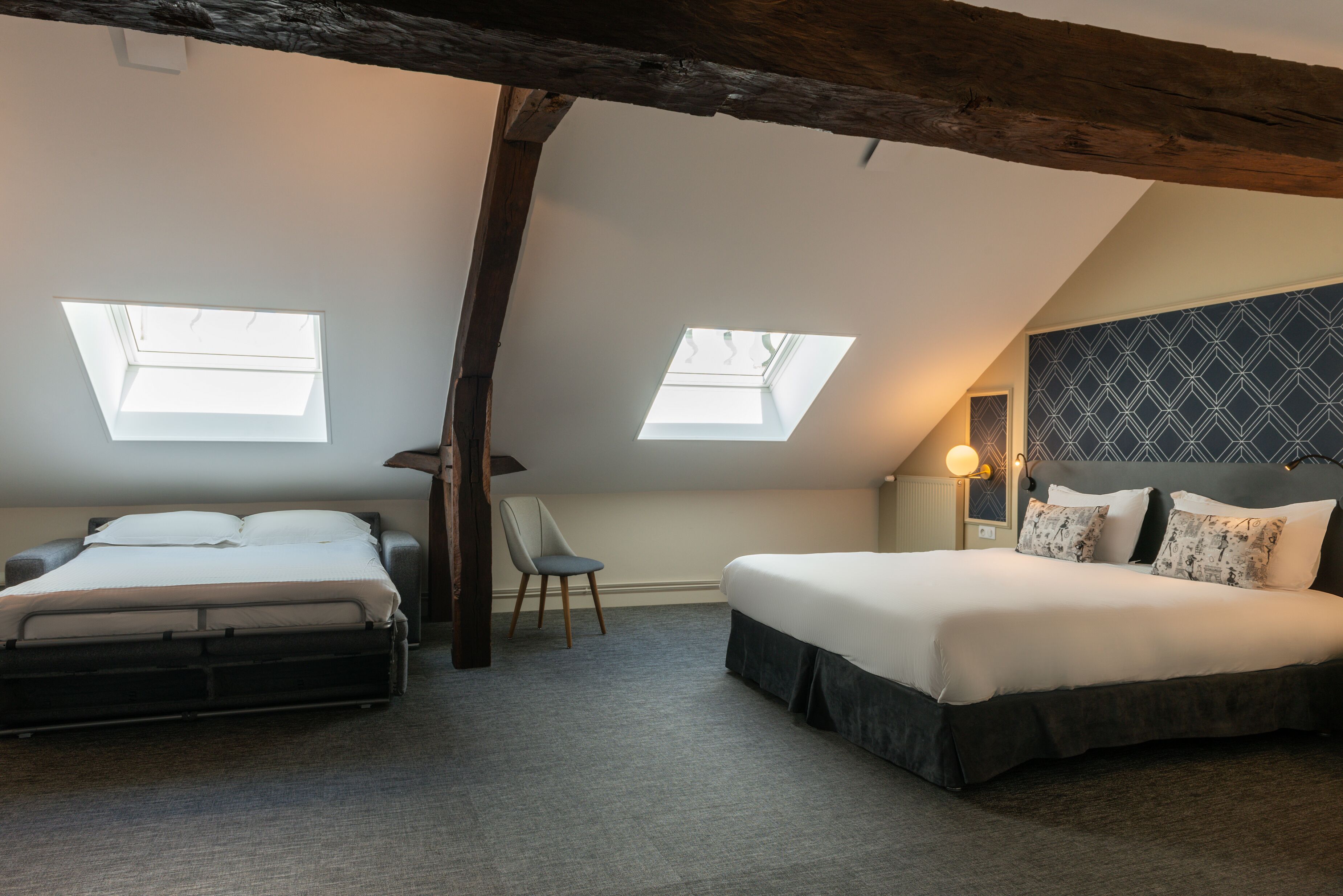 A bedroom with two beds, a skylight, a chair, and a patterned headboard.