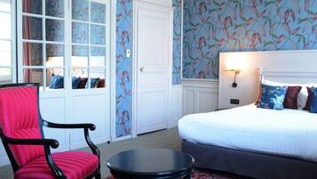 A hotel room with a bed, a red upholstered chair, a small table, and a window with curtains.