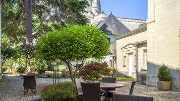 An outdoor dining area with a table set for breakfast, including eggs, bacon, and fruit, with a historic building in the background.