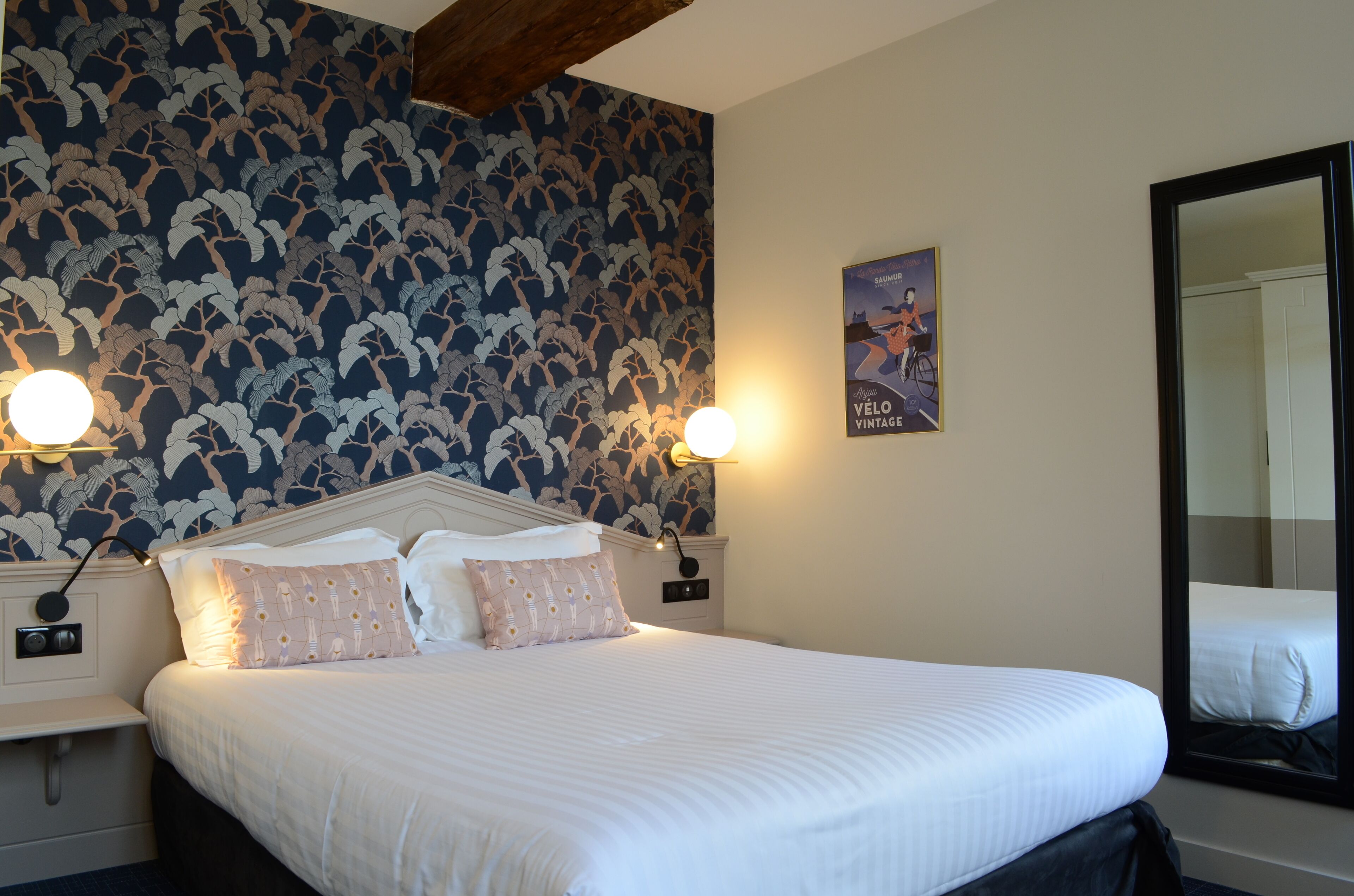 A hotel room with a large bed, two bedside tables, a nightstand, a wall-mounted light, a poster, and a large mirror.