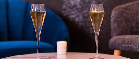 Two champagne flutes on a marble table with a candle in the center, a blue sofa, and a grey armchair in the background.
