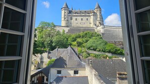 Vista de un edificio que recuerda a un castillo, con una muralla de piedra y torres, visible a través de una ventana abierta.