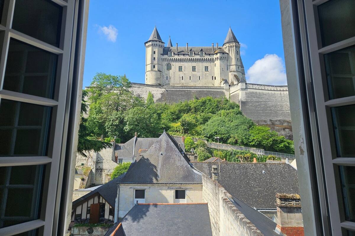 A view of a castle-like building with a stone wall and towers, seen through an open window.