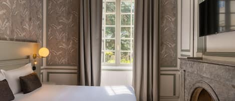 A hotel room with a large bed, a fireplace, a television, and a window with curtains.