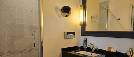 Un baño con ducha, un lavabo doble y un espejo, además de una lámpara de pared.