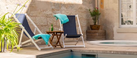 Zona de piscina con dos sillones, una mesita y una botella, y una planta en maceta.