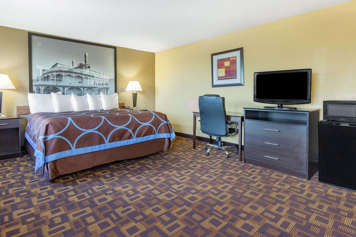 A hotel room with a bed, desk, chair, television, and a patterned carpet.