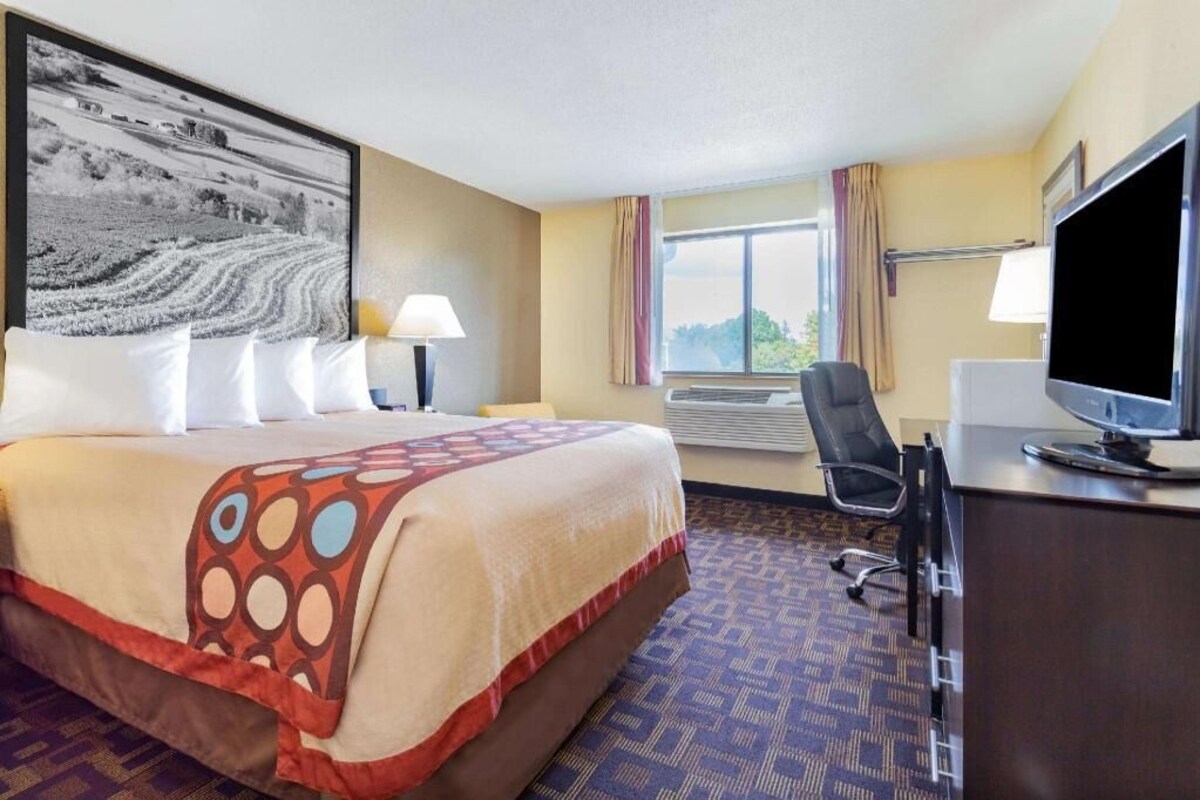 A hotel room with a large bed, a desk with a computer, a chair, and a window with curtains.