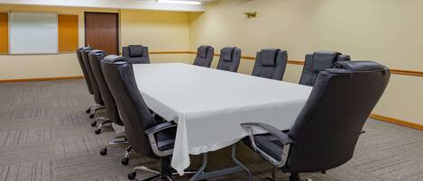 Un salón de conferencias con una gran mesa rectangular, sillas negras, piso alfombrado y una pizarra en la pared.