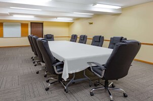 Un salón de conferencias con una gran mesa rectangular, sillas negras, piso alfombrado y una pizarra en la pared.