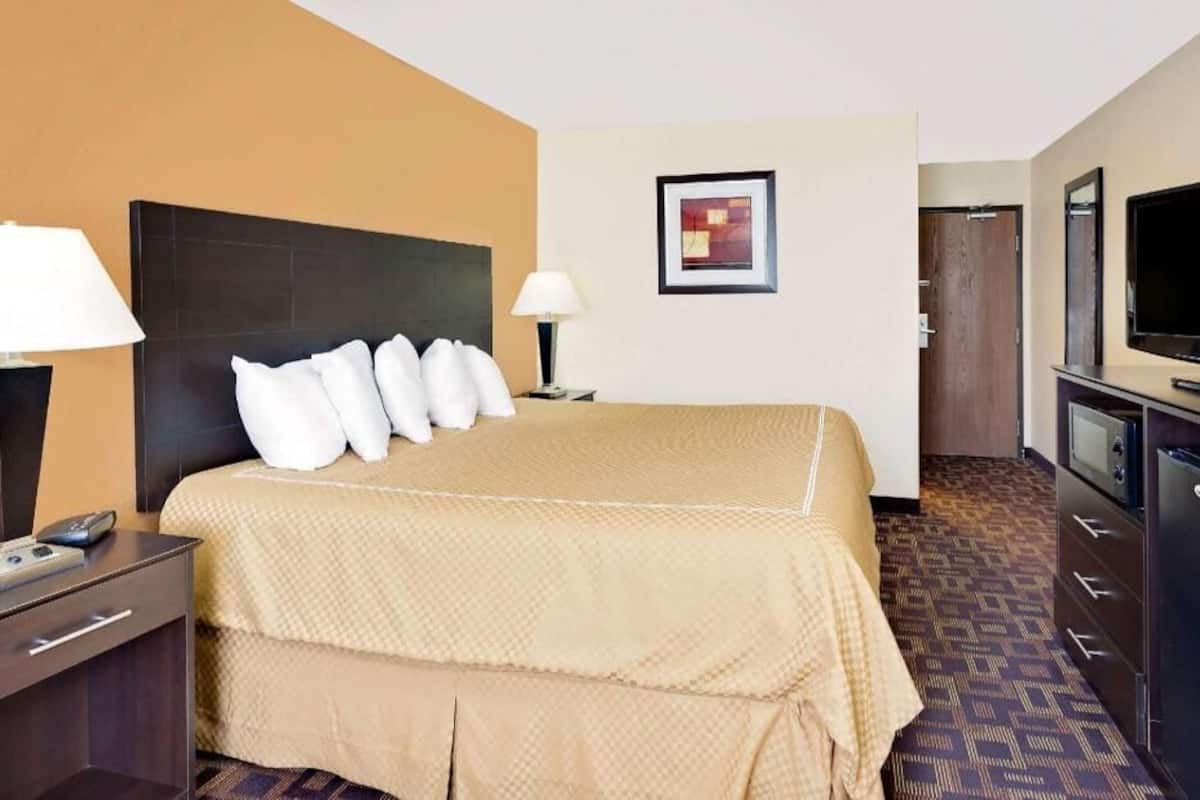 A hotel room with a bed, bedside tables, a TV, and a door.