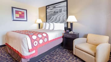 A hotel room with a bed, two bedside lamps, a chair, a nightstand, a framed picture, and a patterned carpet.