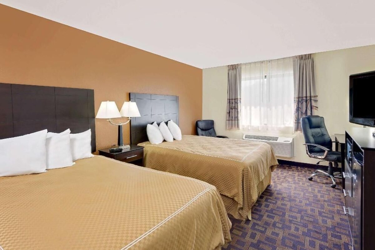 A hotel room with two beds, a desk with a chair, a television, and a window with curtains.