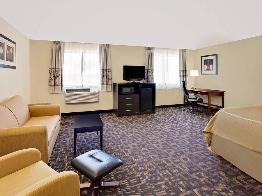 A hotel room with a sofa, a bed, a desk with a computer, a television, and an air conditioning unit.