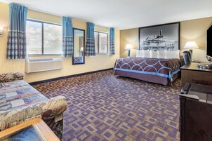 Habitación de hotel con alfombra estampada, cama con colcha estampada, sofá, escritorio con lámpara y un cuadro grande en la pared.