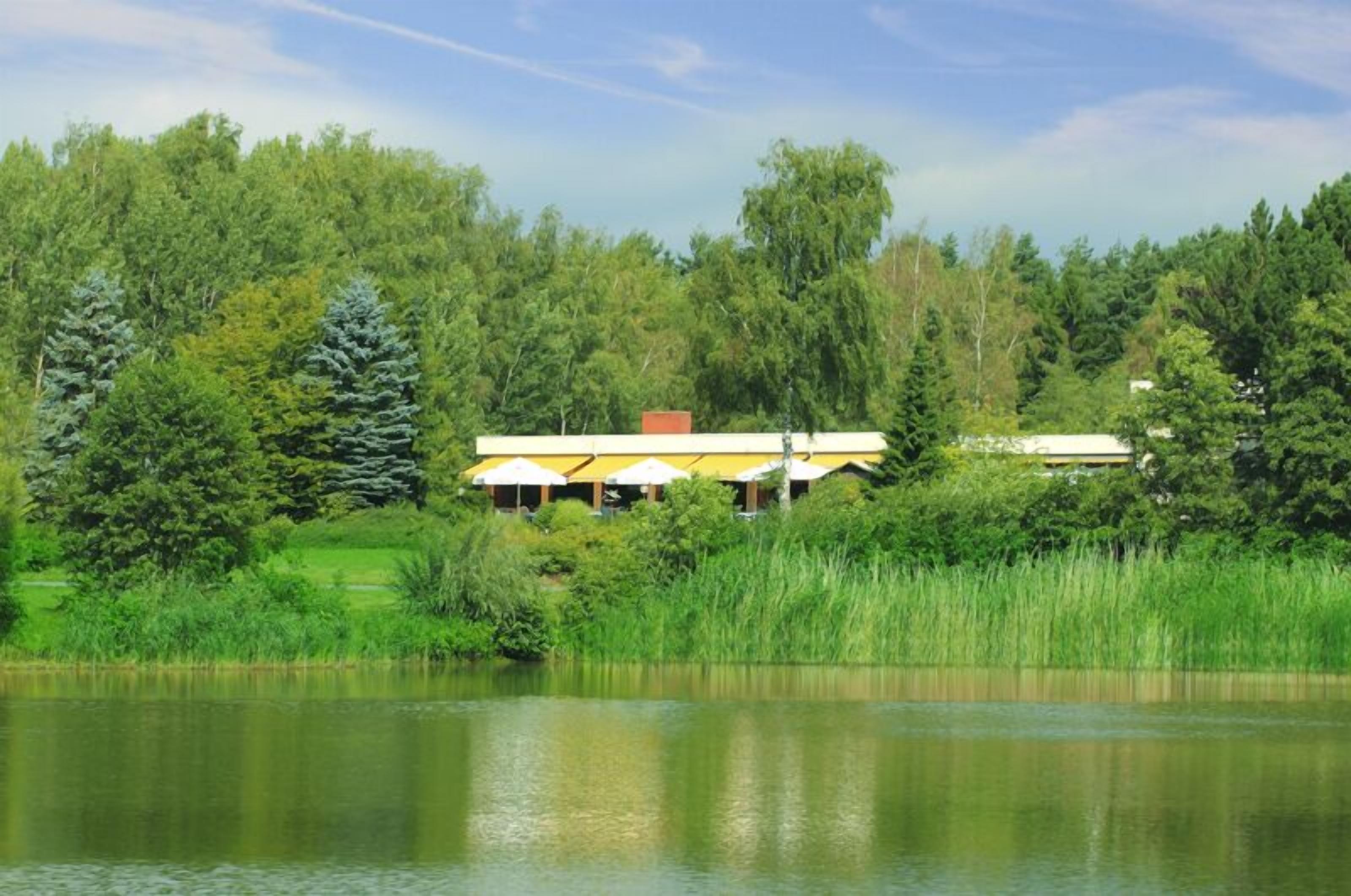 A lakeside building with a yellow roof, surrounded by dense greenery and trees.