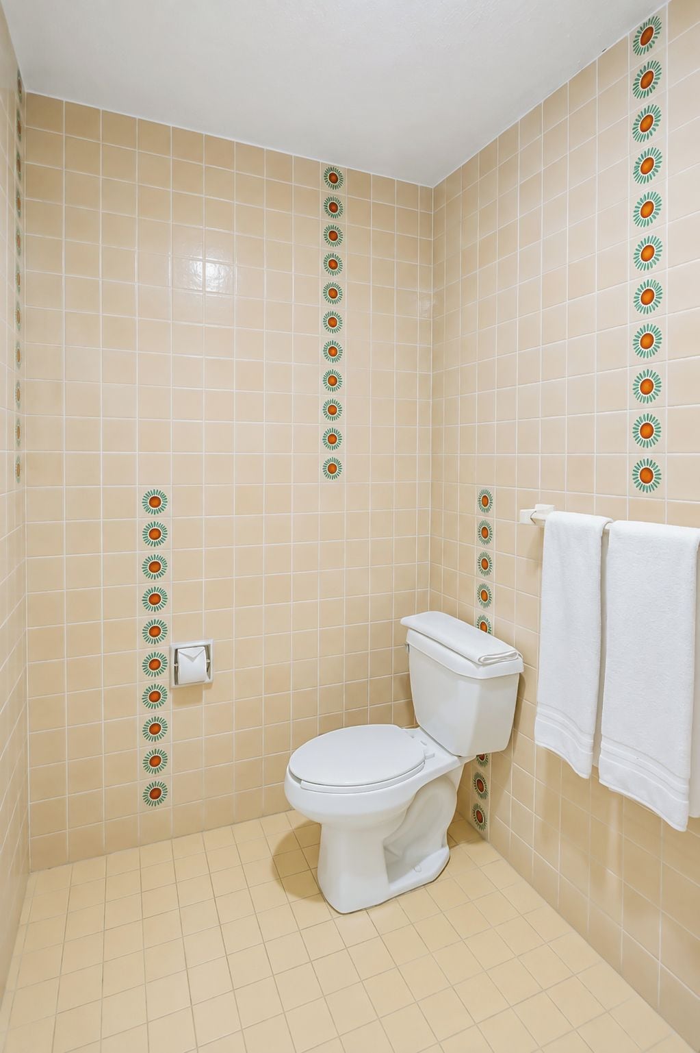 Casa de banho com sanita, um porta-toalhas com duas toalhas e azulejos decorativos nas paredes.