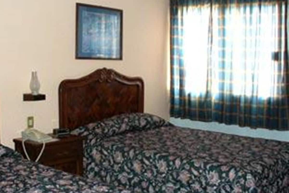 A bedroom with a wooden bed, a nightstand, a framed picture on the wall, and a window with curtains.