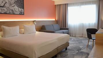 Ein Hotelzimmer mit einem großen Bett, einer Couch, einem Schreibtisch und einem Sessel.