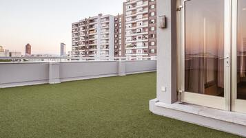 A rooftop terrace with artificial grass, a sliding glass door, and a view of high-rise residential buildings.