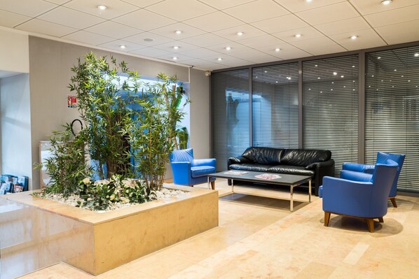 A modern reception area with a reception desk, a large indoor plant, blue seating, and a black leather couch.