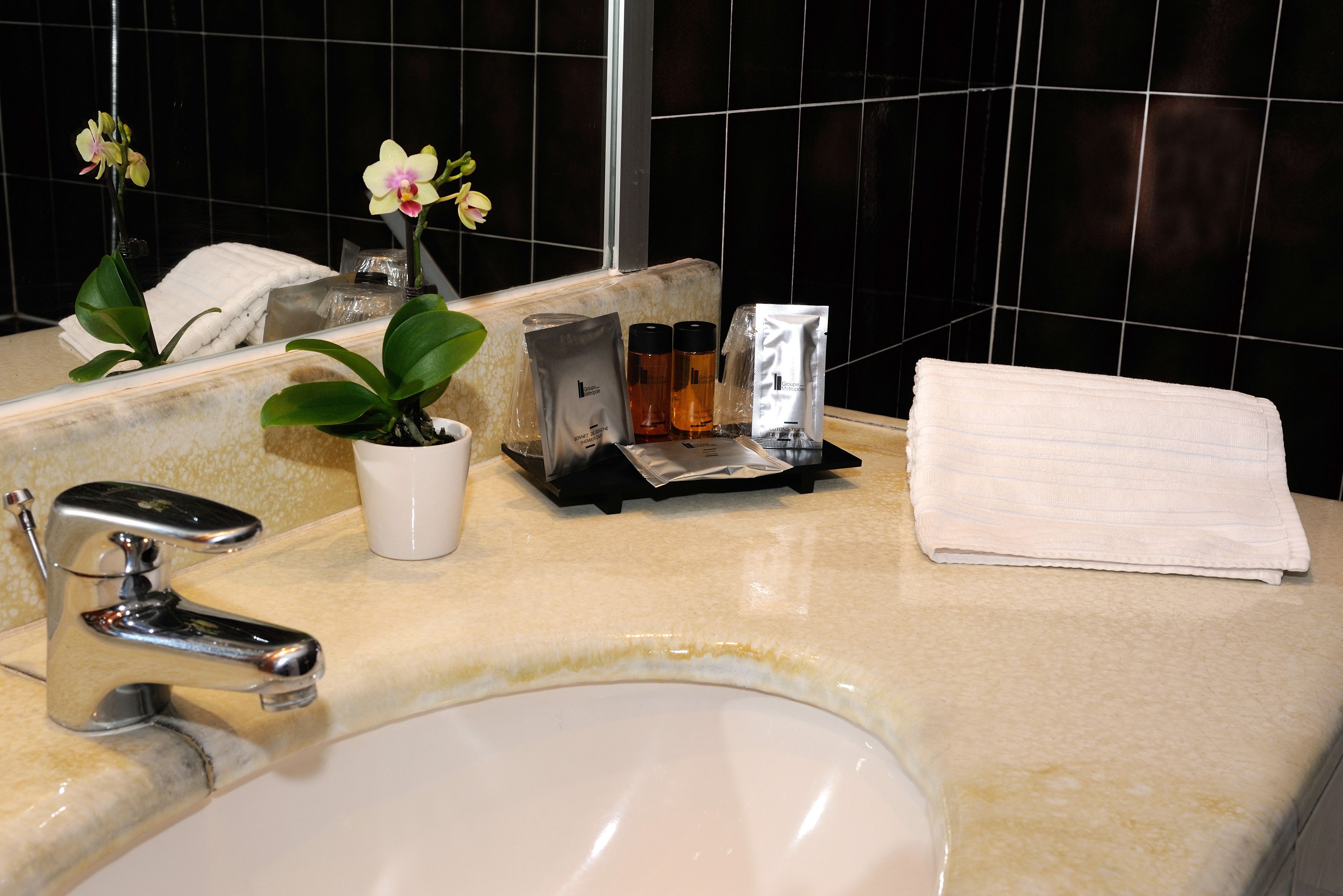 A bathroom sink with a mirror, a white towel, a potted orchid, and toiletries on the counter.