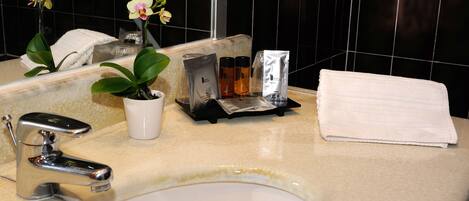A bathroom sink with a mirror, a white towel, a potted orchid, and toiletries on the counter.