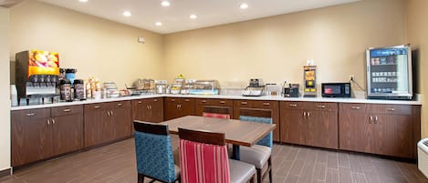 A hotel kitchen with a dining area, equipped with a coffee machine, a refrigerator, and a microwave.