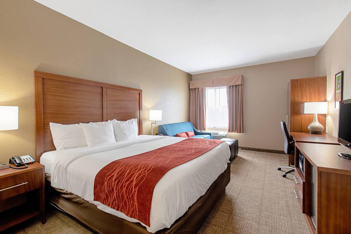 A hotel room with a large bed, a desk, a chair, a TV, and a window with curtains.