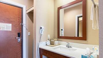 Un baño de hotel con una puerta de madera, un lavabo blanco, un espejo, un secador de pelo y un perchero para toallas.