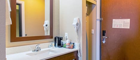 A bathroom with a sink, mirror, hair dryer, and an emergency evacuation plan on the door.