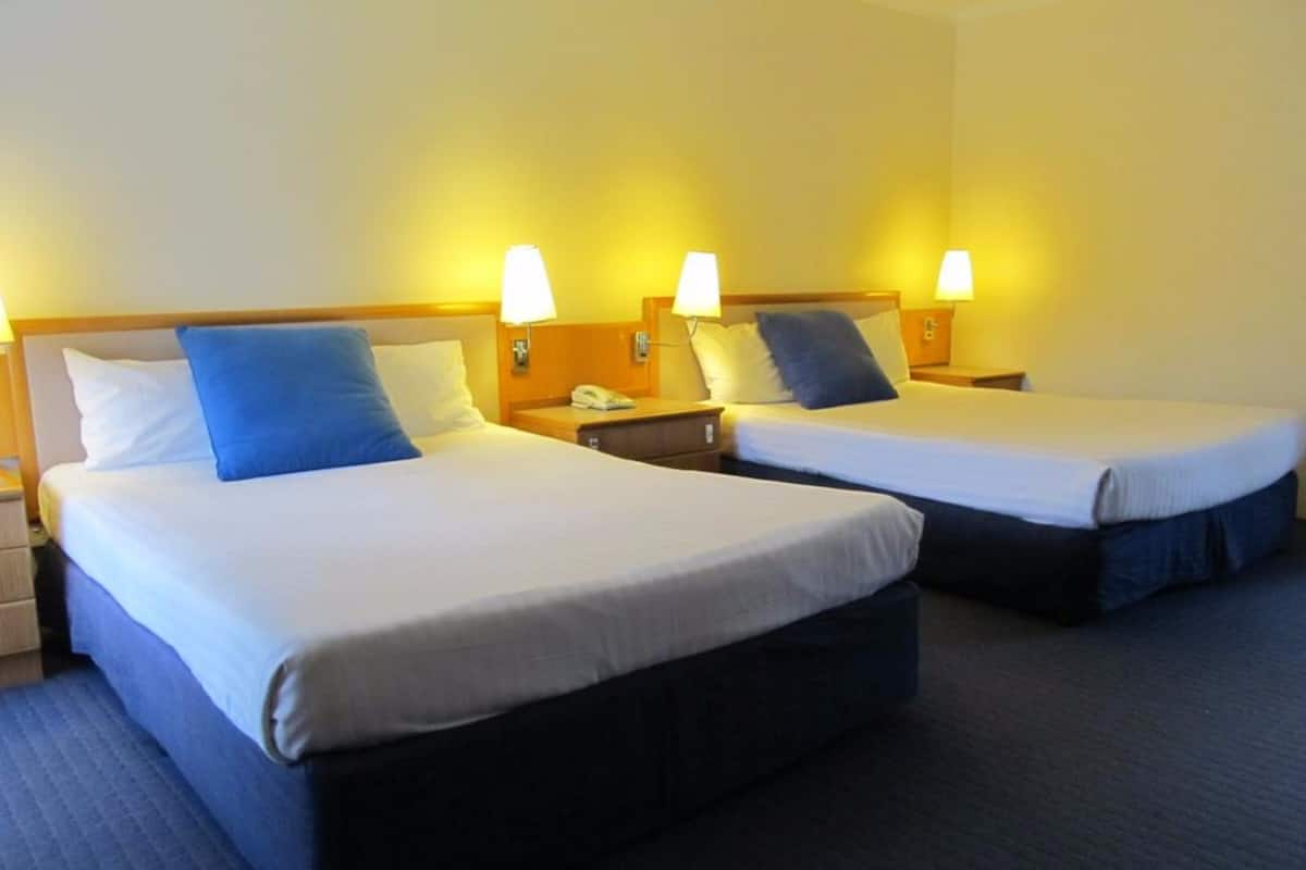 Dos camas individuales con cabeceras, mesitas de noche con lámparas y suelo alfombrado en una habitación de hotel.