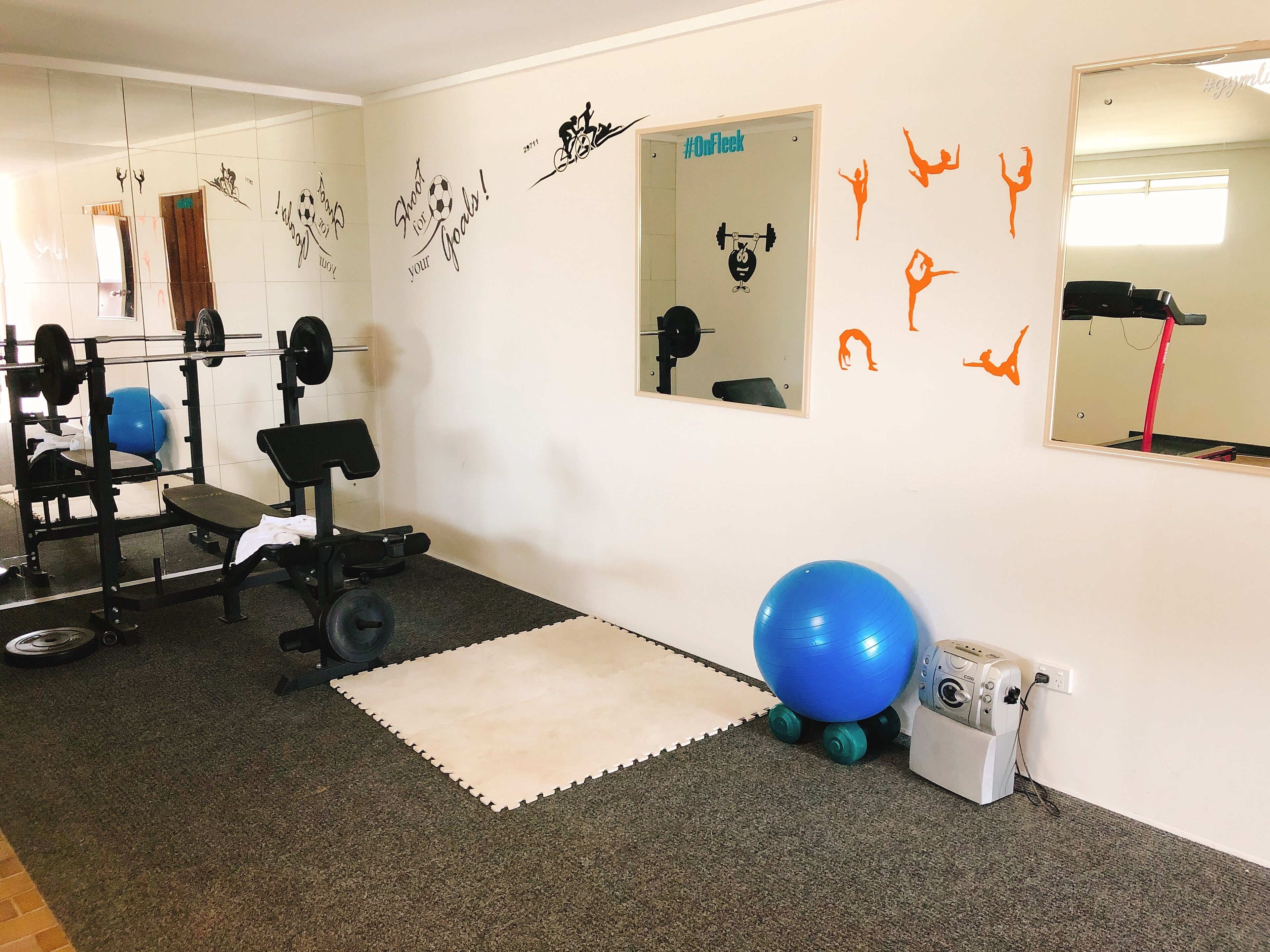 A gym with exercise equipment, a mirror, motivational wall decals, and a blue exercise ball.