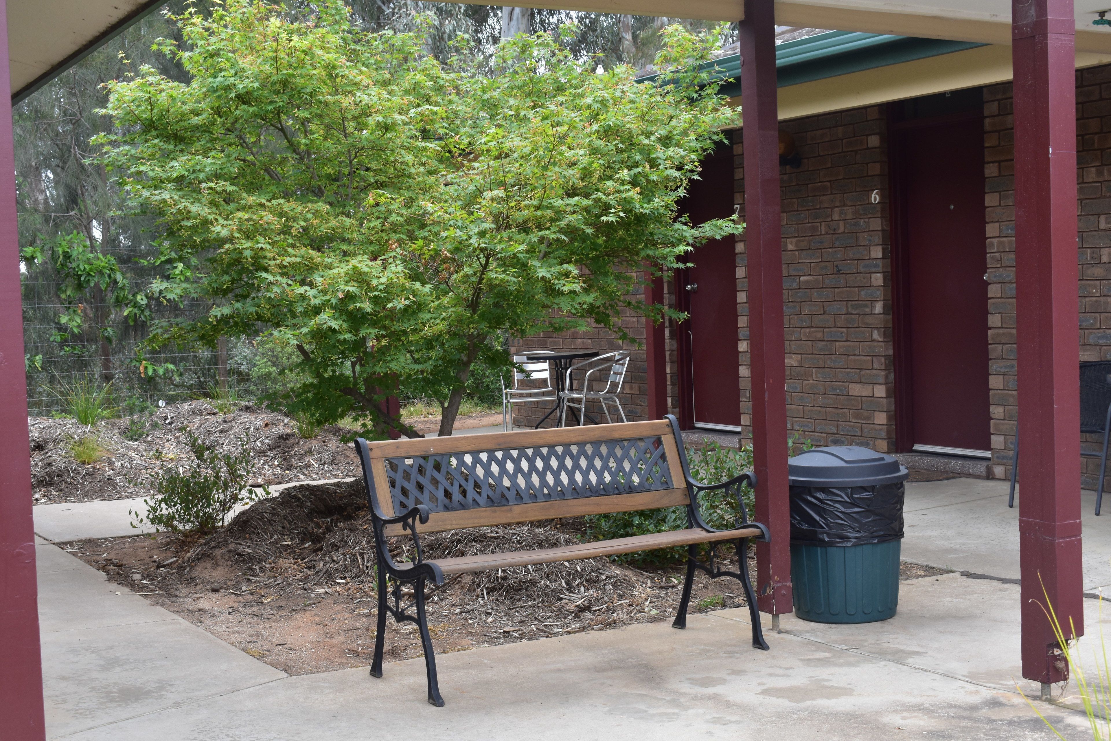 A wooden bench with a lattice backrest, a trash bin, and a brick building in the background.