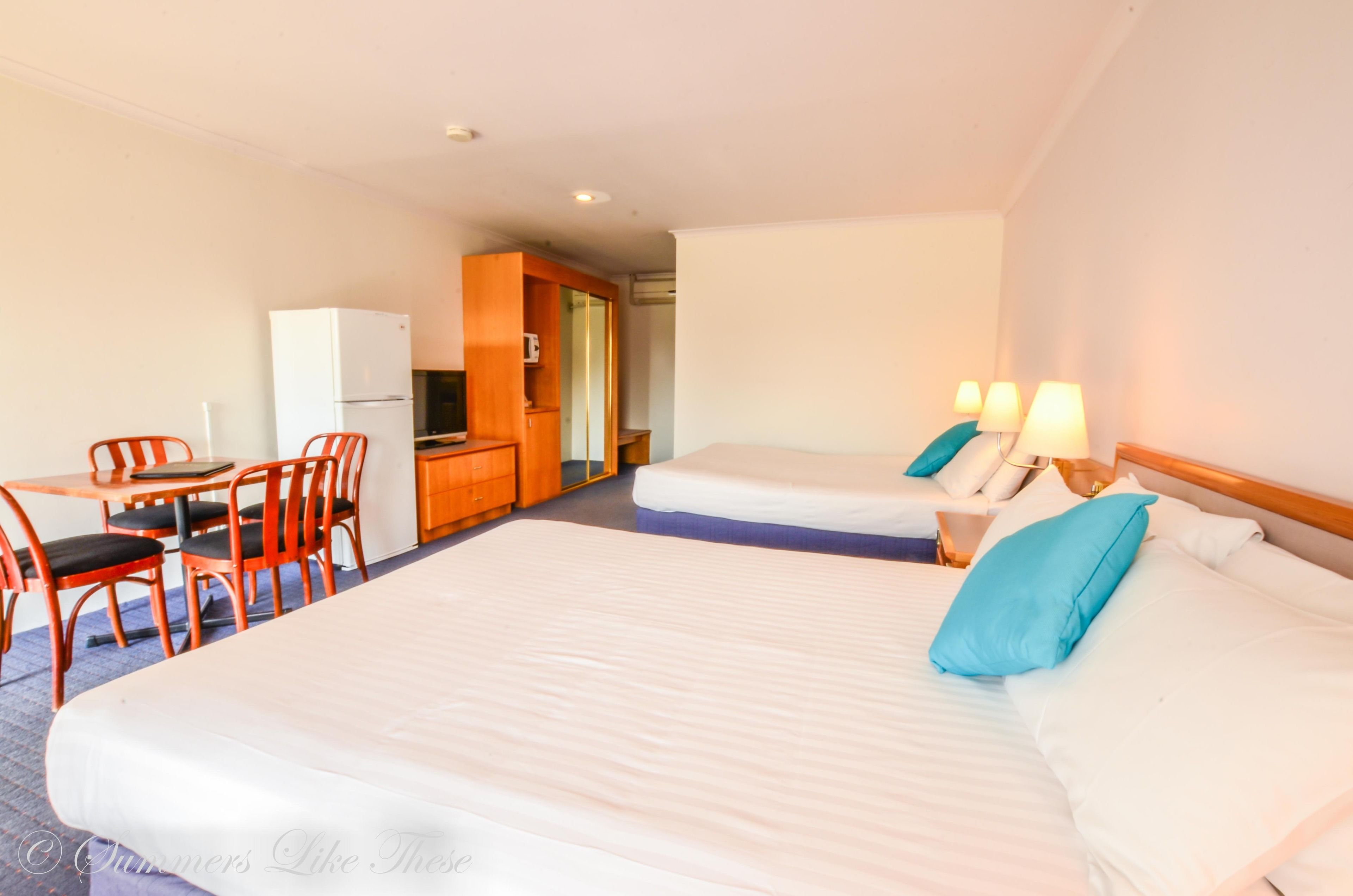 A hotel room with two beds, a small kitchenette, a dining area with a table and chairs, and a separate bathroom.