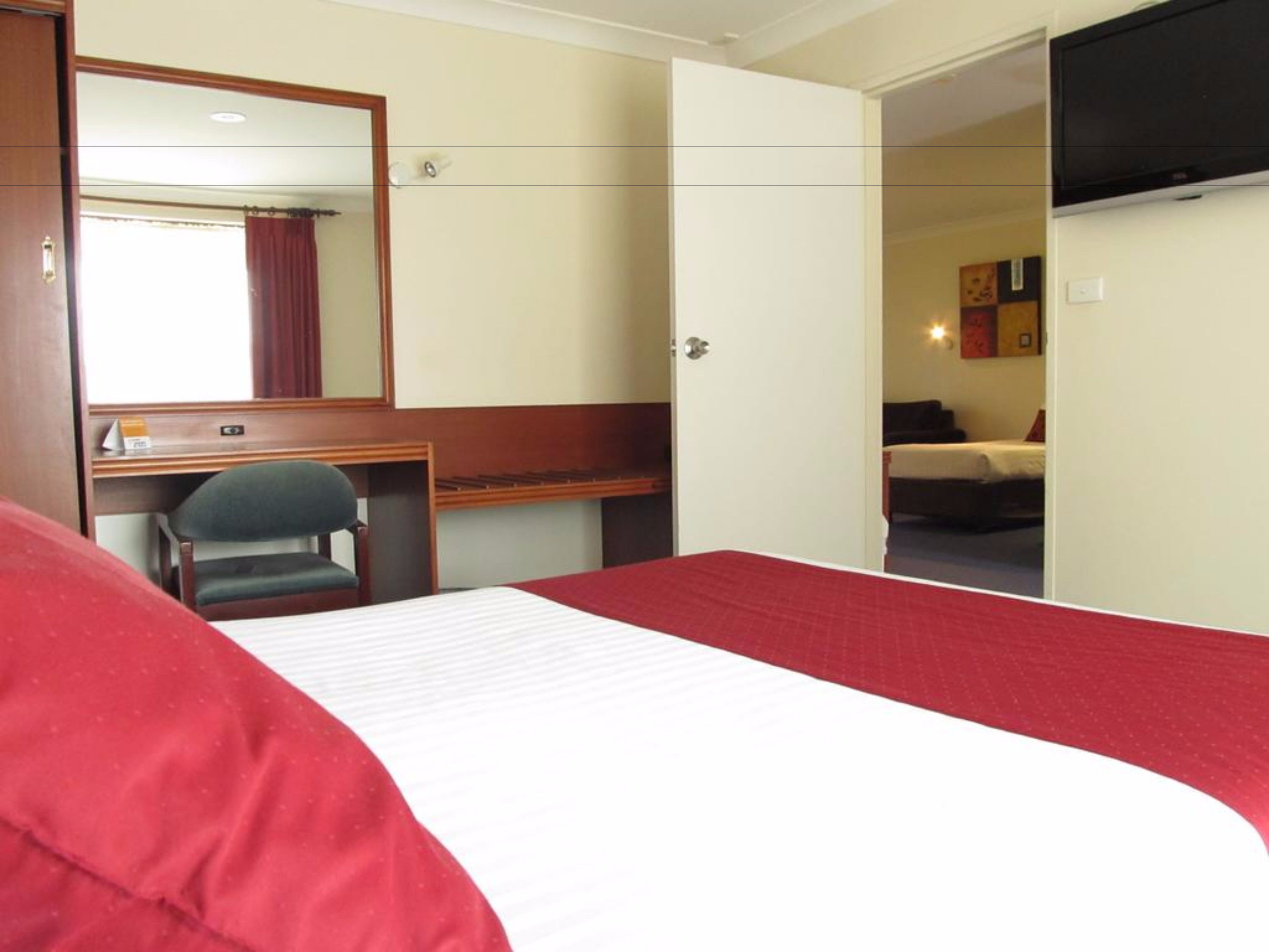 Une chambre d’hôtel équipée d’un lit, d’un bureau, d’une chaise, d’une télévision et d’une porte donnant sur une autre pièce.