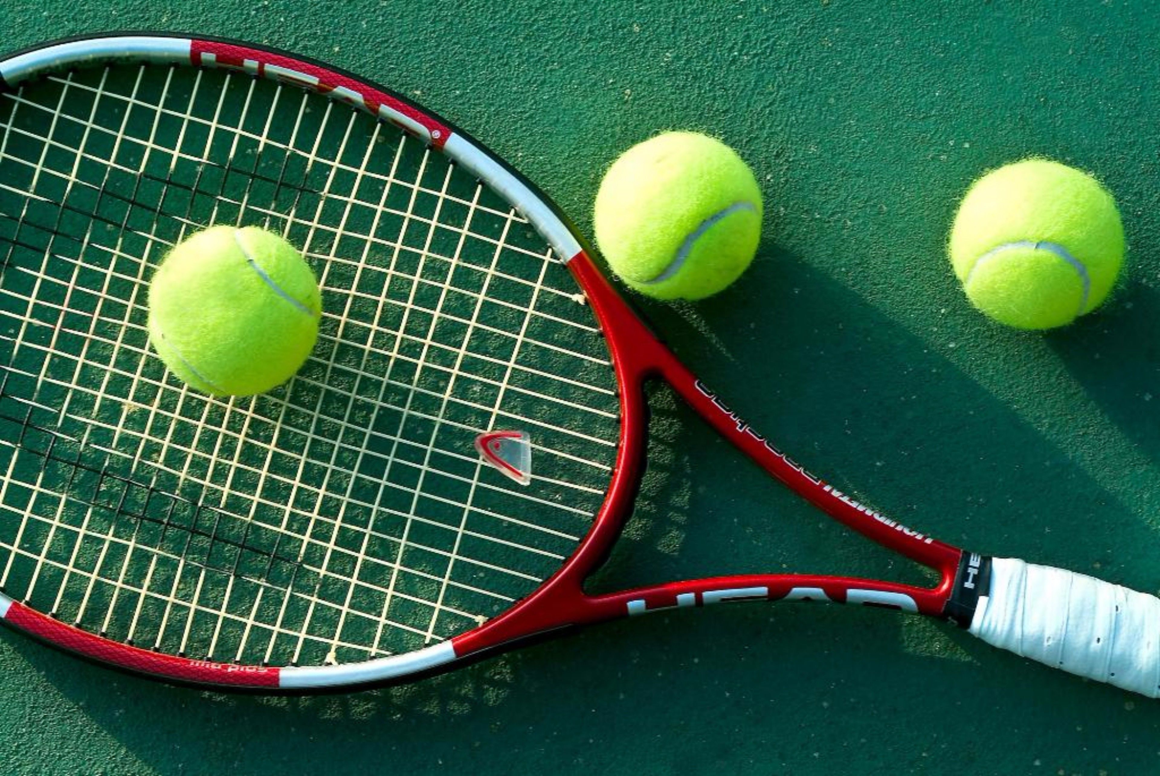 Een tennisracket en twee tennisballen op een groene baan.