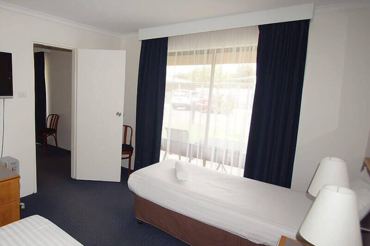 Una habitación de hotel con una cama individual, una silla, un escritorio con teléfono y una ventana con cortinas.