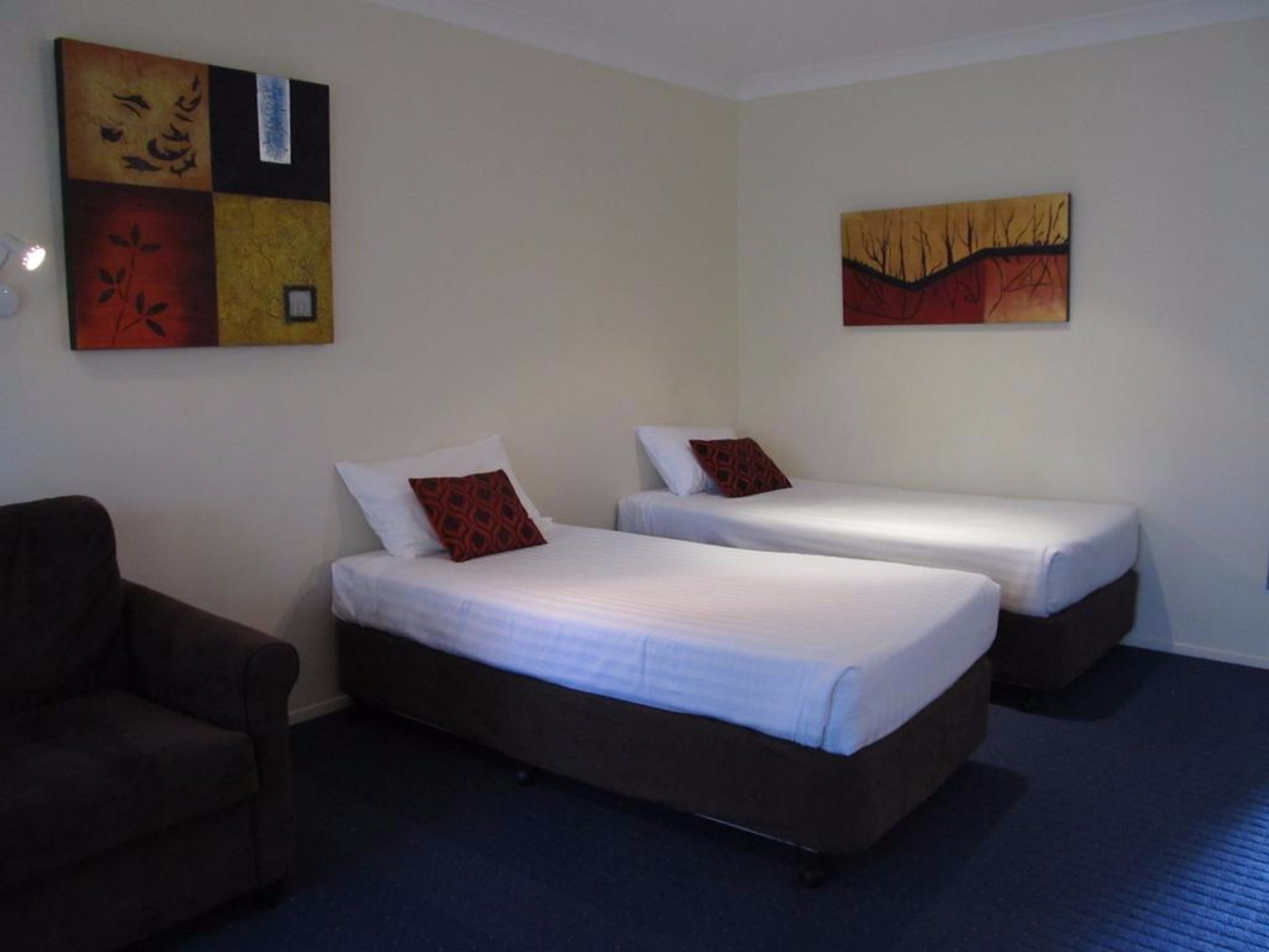 Habitación de hotel con dos camas individuales, un sofá y obras de arte en las paredes.