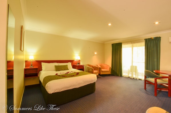 Habitación de hotel con una cama grande, dos mesitas de noche, una silla, una mesita pequeña y un ventanal con cortinas.